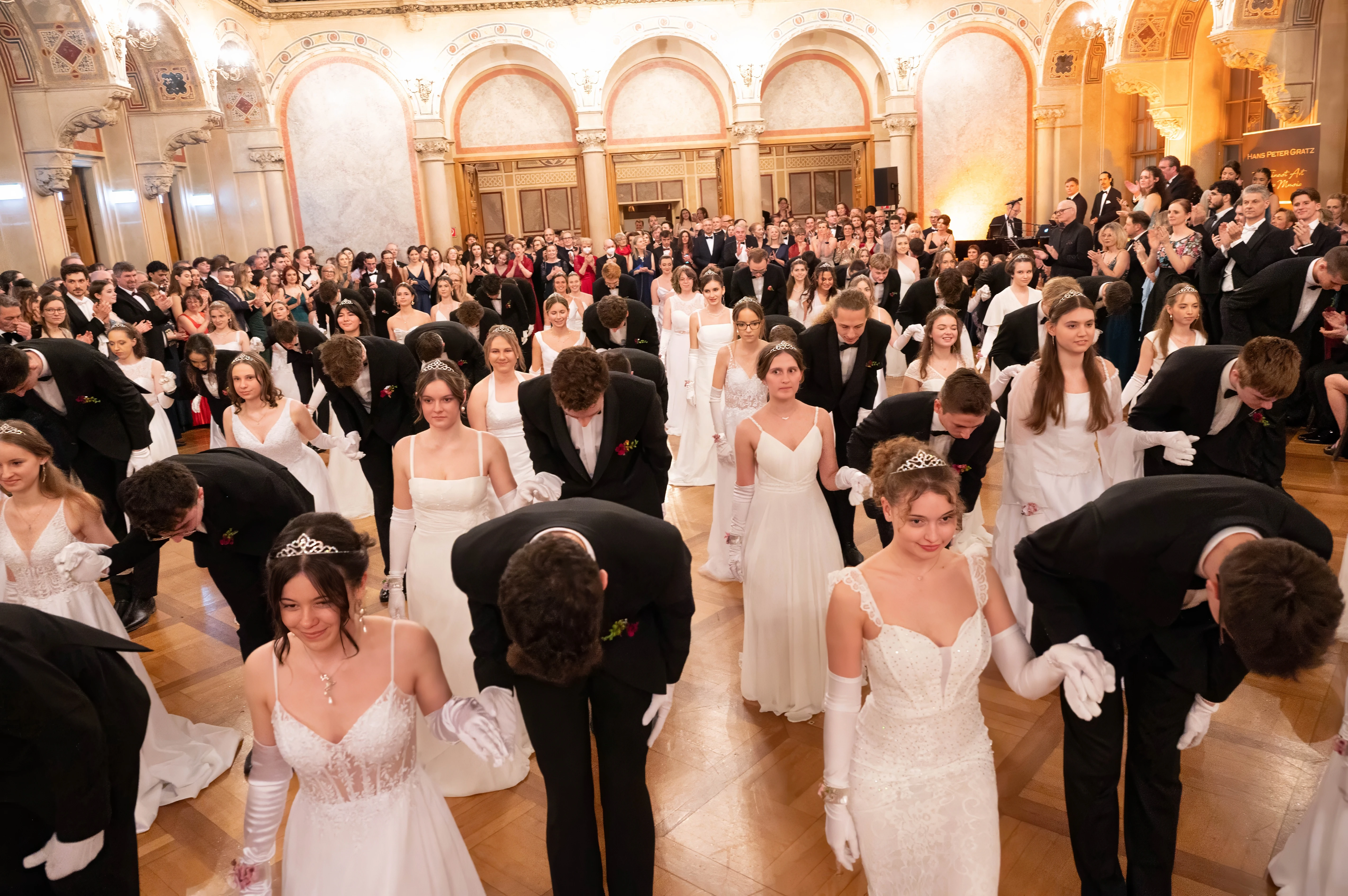Ballsaal mit Jugendlichen in Ballkleidern und Anzügen, die sich verbeugen.